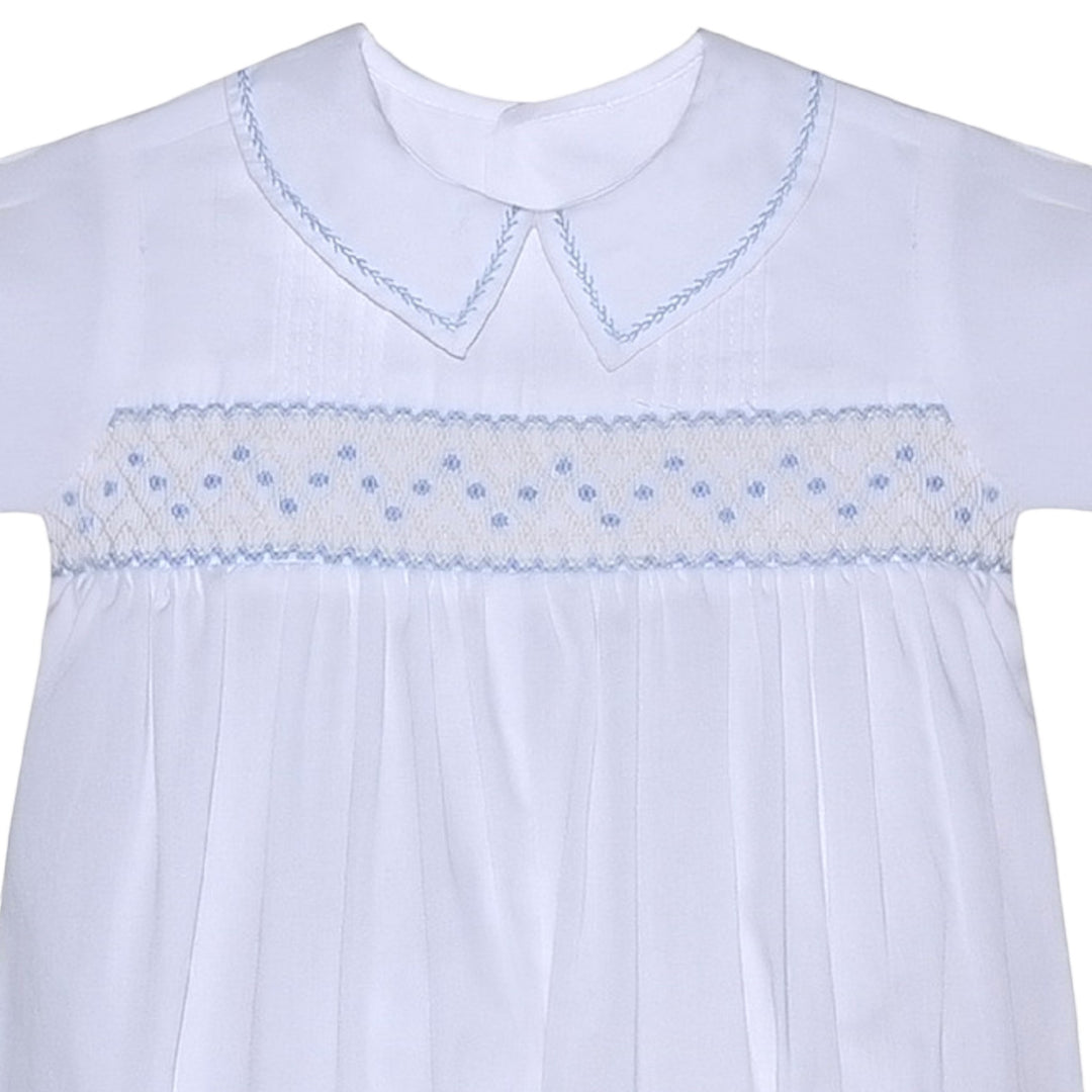 That Store white baby romper with blue geometric smocking, peter pan collar, and delicate embroidery details.