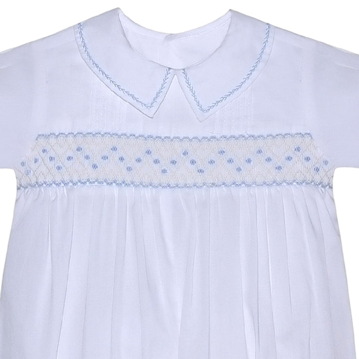 That Store white baby romper with blue geometric smocking, peter pan collar, and delicate embroidery details.