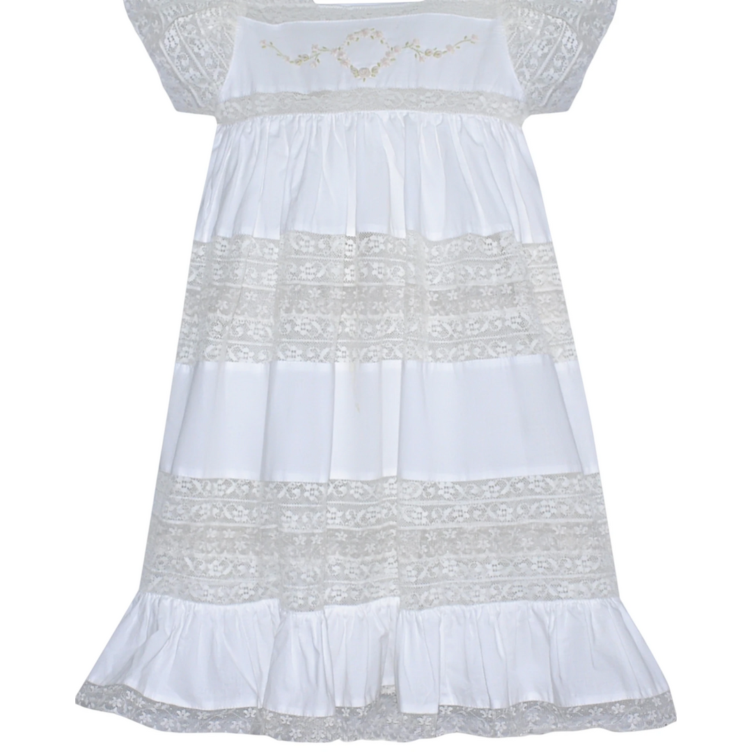 That Store white cotton heirloom dress featuring intricate lace panels and delicate floral embroidery on the bodice.