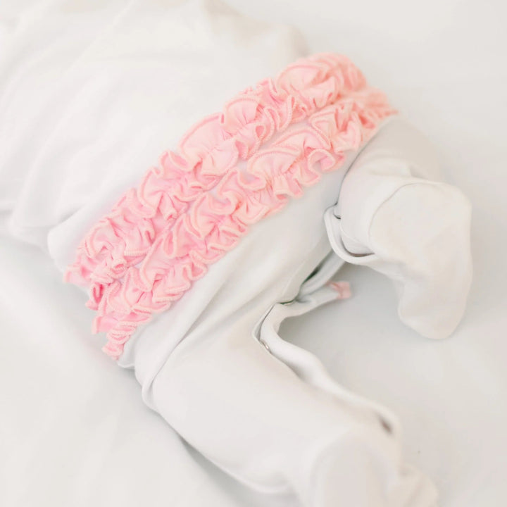 That Store white cotton baby footie featuring a decorative pink ruffled back detail and soft snap closures.