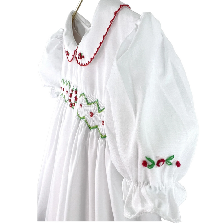 That Store white holiday dress for girls featuring red and green smocking, embroidery, and a peter pan collar.