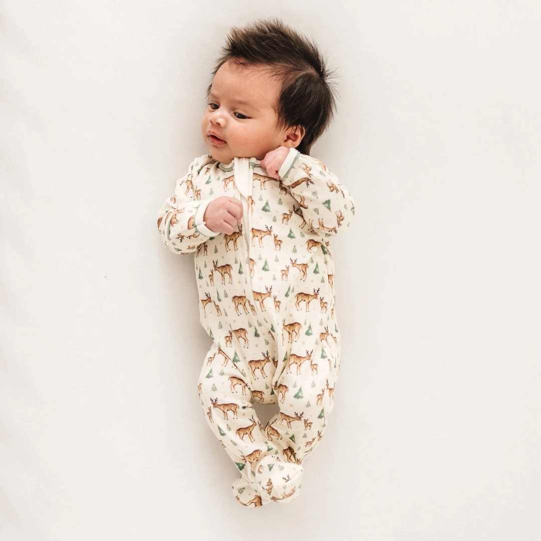 Baby wearing a That Store ivory Pima cotton footie with a woodland deer and tree print and moss green trim.